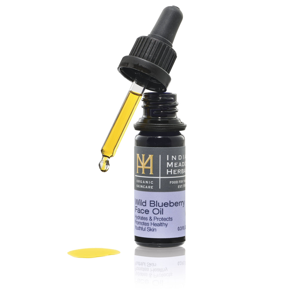 Open bottle of Wild Blueberry Face Oil with a drop of oil on white background